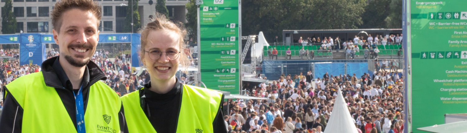 Das Bild zeigt einen Sicherheitsmager und eine Sicherheitsmanagerin der FAN ZONE in Hamburg. Im Hintergrund sieht man Fans im Bereich des Public Viewings