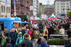 Das Bild zeigt den Hamburger Jungfernstieg mit Food Trucks, Besuchenden und Sitzgelegenheiten während der Veranstaltung zum Tag der Deutschen Einheit 2023 in Hamburg.